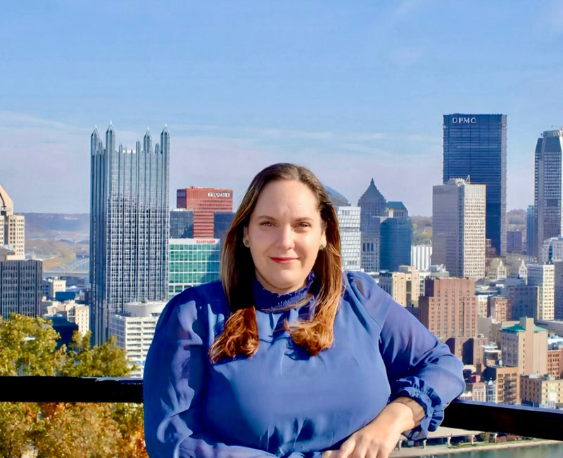 Woman in a blue shirt standing in front of overlook pittsburgh city skyline on mt. washington